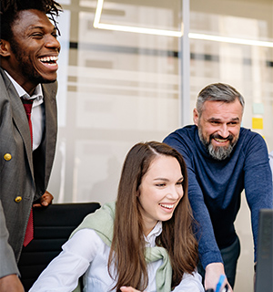 Three colleagues smiling together around a computer in an office